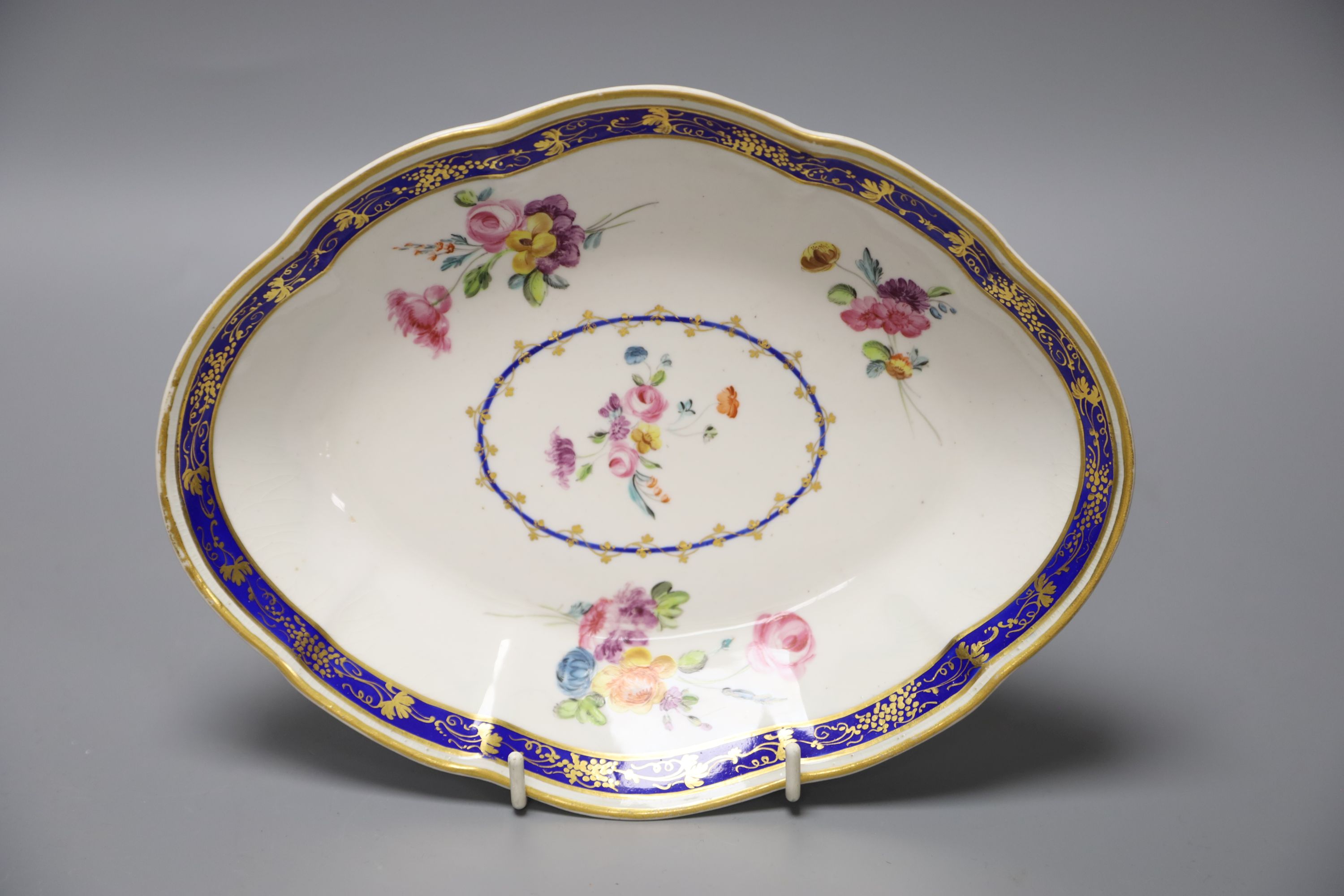 A Chelsea Derby oval dish painted with flowers in the manner of Withers under a Smiths blue and gilt border, blue crown D mark, length